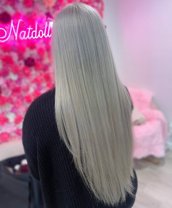 Long platinum-blonde hair styled sleek and straight, against a pink flower wall